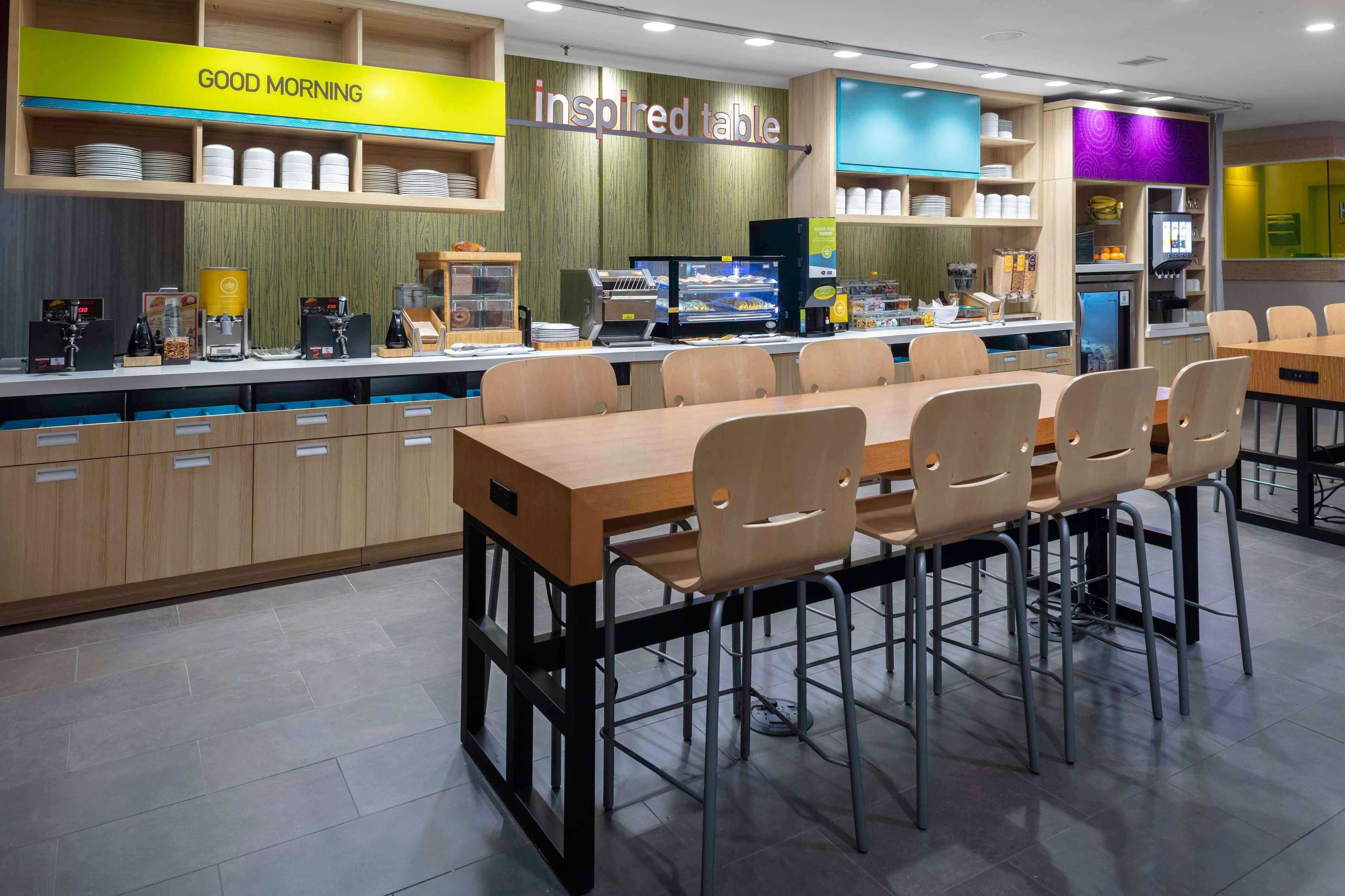 Un restaurante moderno con barra de desayuno, diversas opciones de asientos y variedad de estaciones de comida y bebidas.