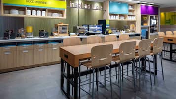 Un restaurante moderno con barra de desayuno, diversas opciones de asientos y variedad de estaciones de comida y bebidas.