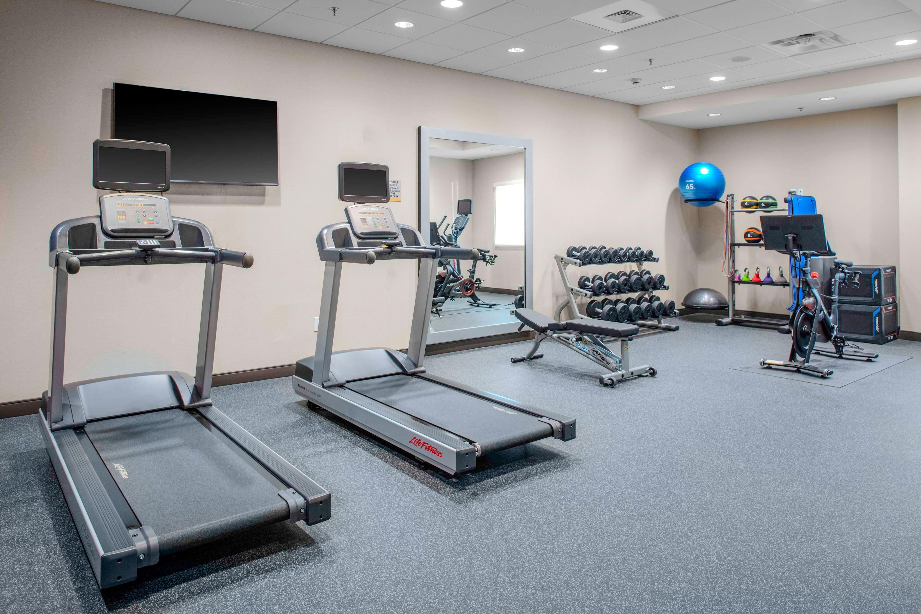 Ein Fitnessraum mit Laufbändern, einem Spiegel, einem Fernseher und einer Hantelbank.