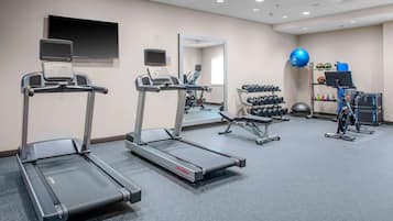 Ein Fitnessraum mit Laufbändern, einem Spiegel, einem Fernseher und einer Hantelbank.