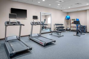 Un gimnasio con cintas de correr, un espejo, un televisor y un estante con mancuernas.