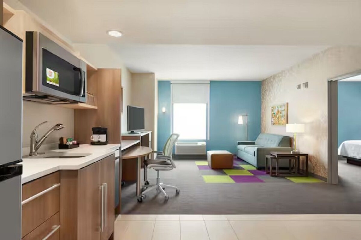 Una habitación de hotel compacta con kitchenette, un sofá, un escritorio y un televisor.