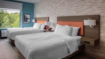 A hotel room with two beds, a large window, and a view of greenery.