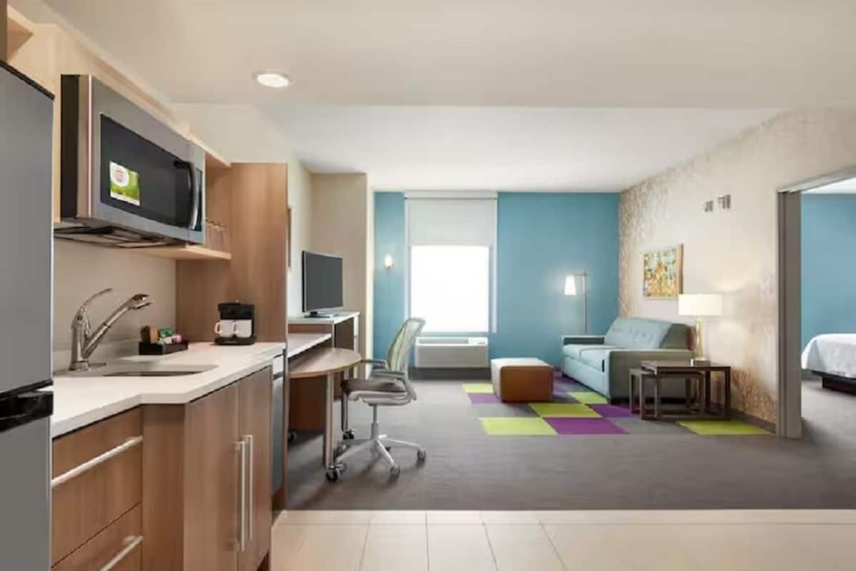 A compact hotel room with a kitchenette, a sofa, a desk, and a television.