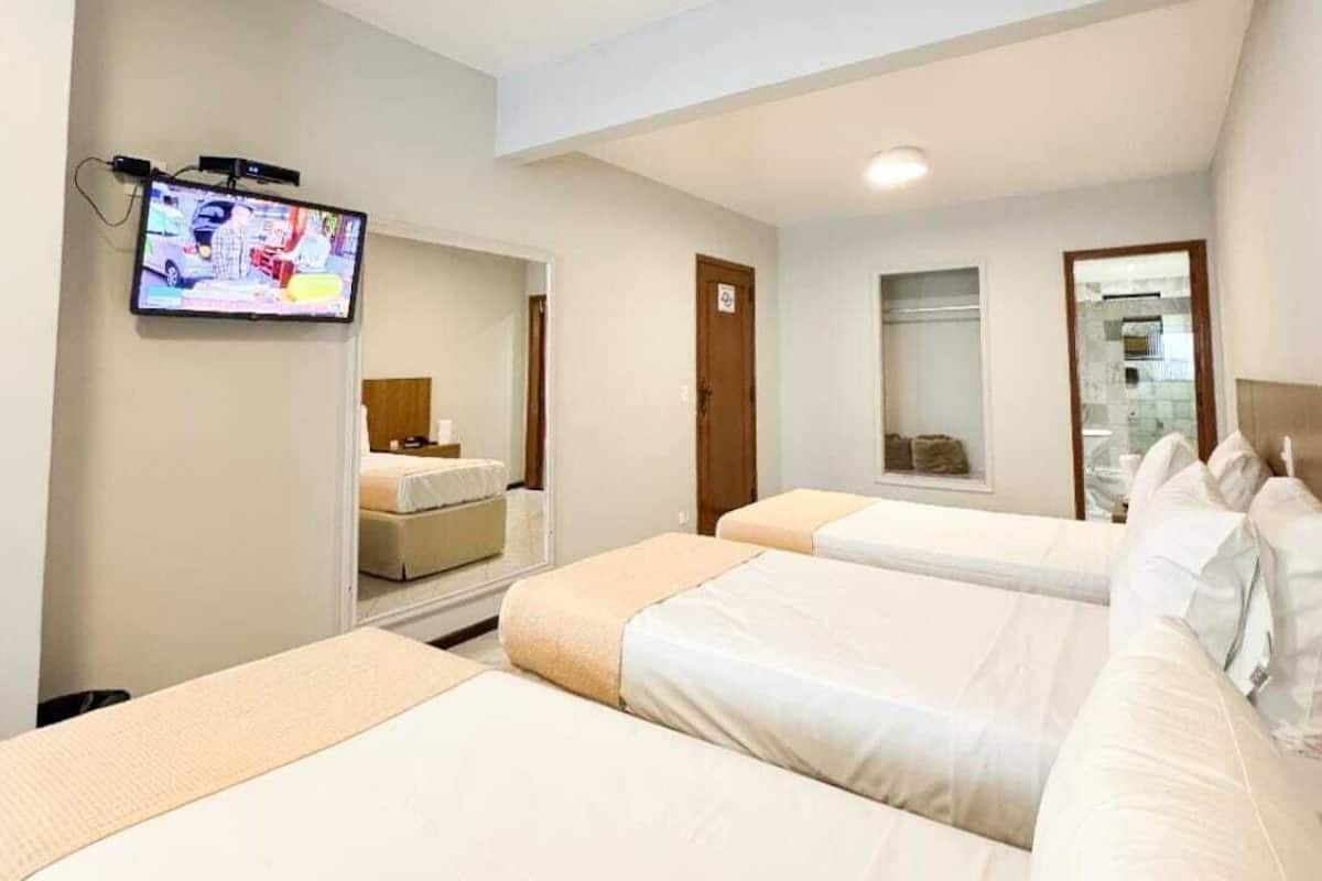 Habitación de hotel con dos camas, un televisor montado en la pared y un baño pequeño con espejo.