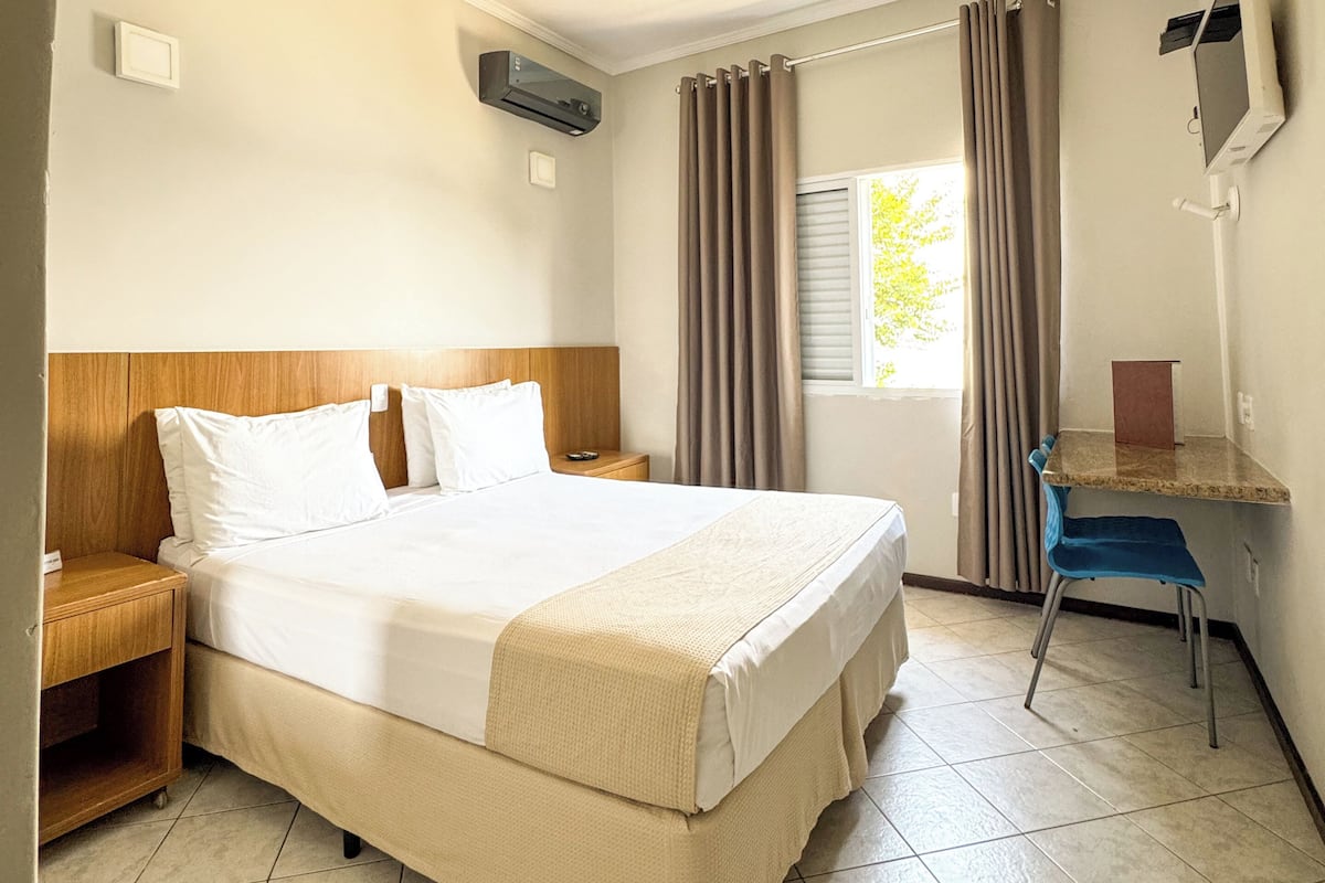 Habitación de hotel con una cama grande, un escritorio, una silla, un televisor y una ventana con cortinas.