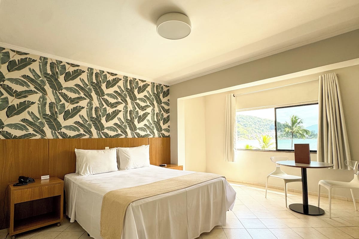 Una habitación de hotel con cama, mesita de noche y vistas al exterior.