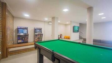 A pool table with a green felt surface, two arcade machines, and a television on the wall.