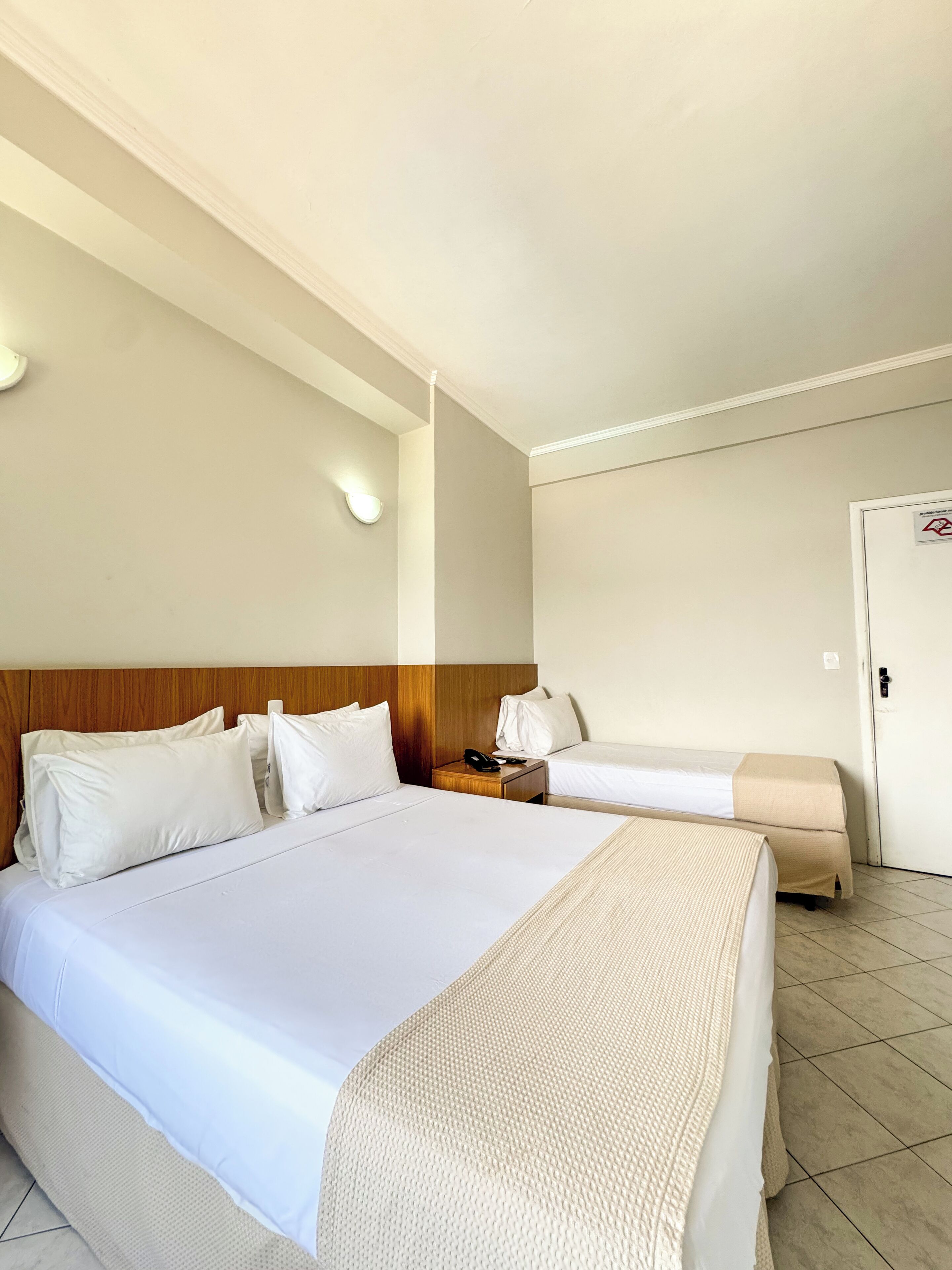 Habitación de hotel con dos camas, cabecera de madera, mesita de noche con teléfono y puerta con cerradura de seguridad.