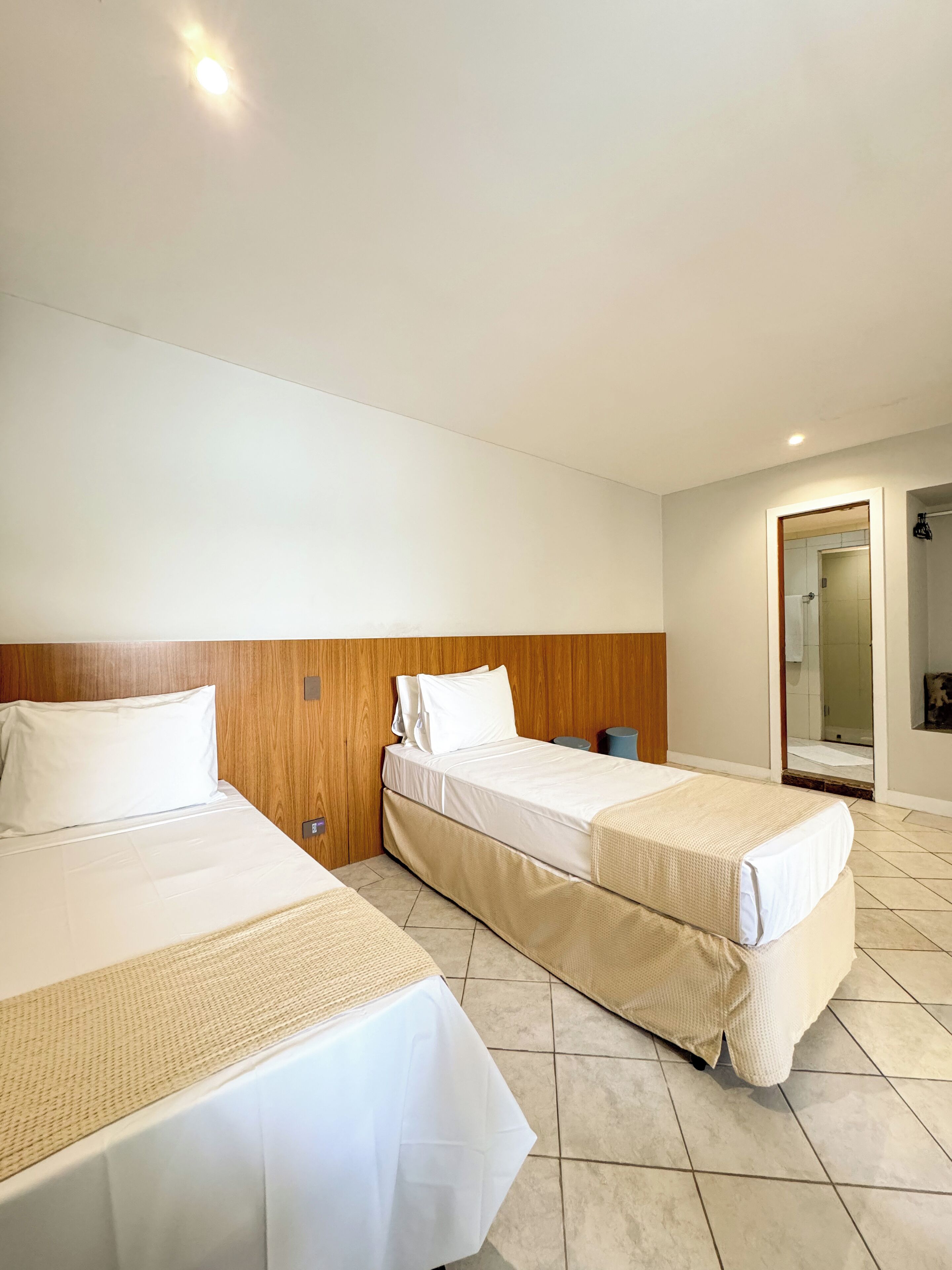 Une chambre d’hôtel avec deux lits, une tête de lit en bois, une petite table et un miroir.