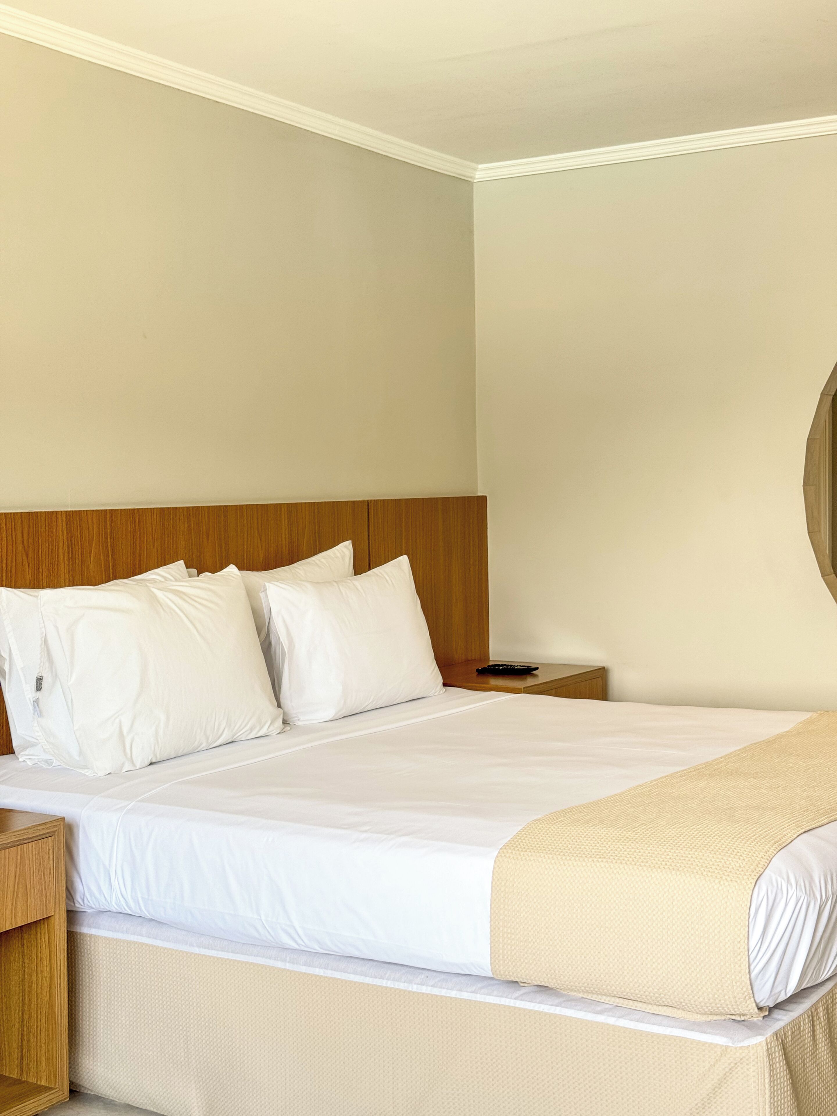 Una habitación de hotel con una cama grande, cabecera de madera, ropa de cama blanca y una mesita de noche pequeña.