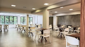 Un espacio interior amplio con varias mesas y sillas, grandes ventanales que ofrecen vistas a zonas verdes, y una decoración moderna con colores neutros.