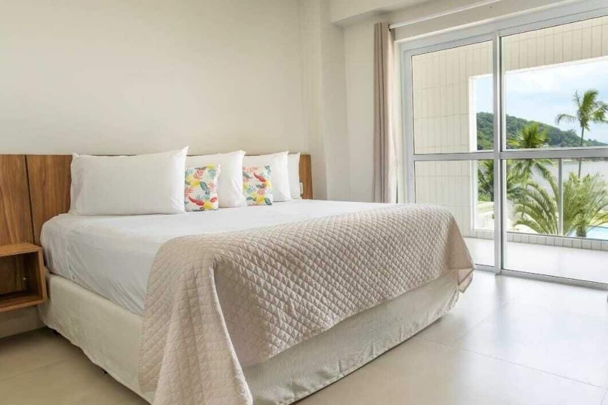 Un dormitorio amplio con una cama grande, cabecera de madera y vista a palmeras a través de una puerta corrediza de vidrio.