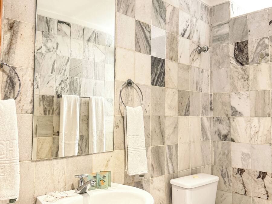 Un baño con pared de azulejos de mármol, un lavamanos, un inodoro y dos toallas colgadas de ganchos.