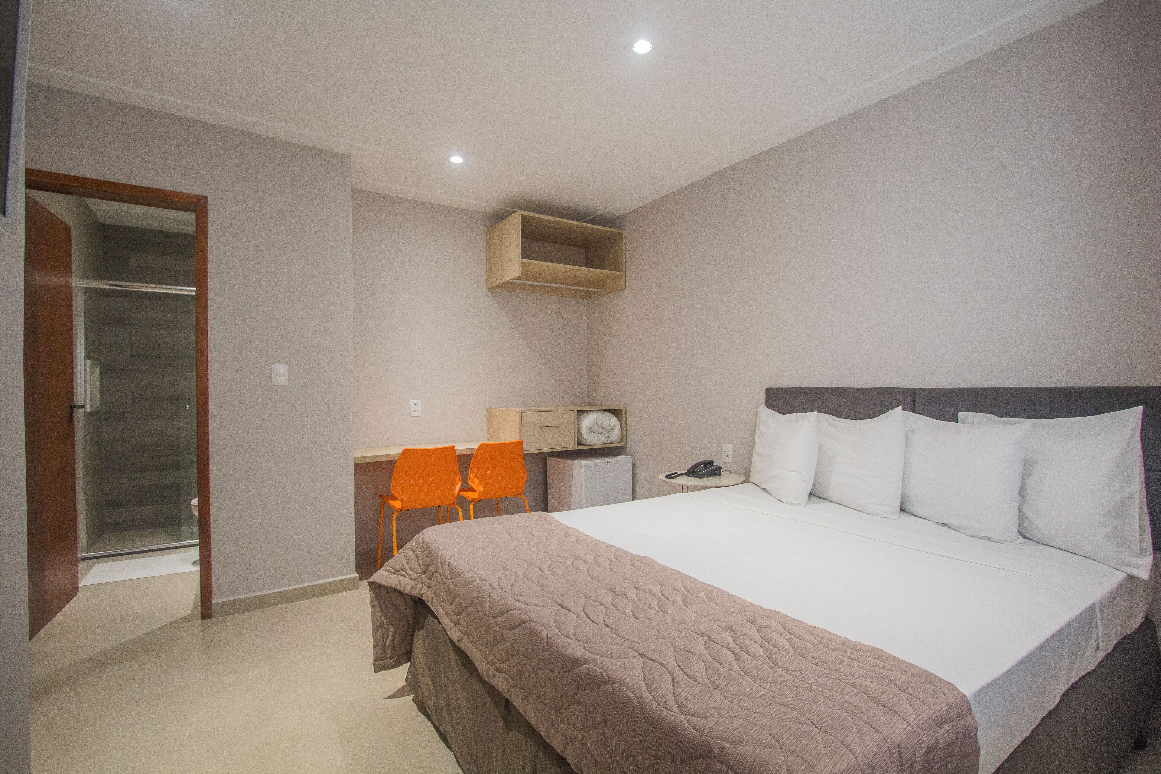 Un dormitorio con una cama grande, dos sillas, un escritorio pequeño y una estantería empotrada.