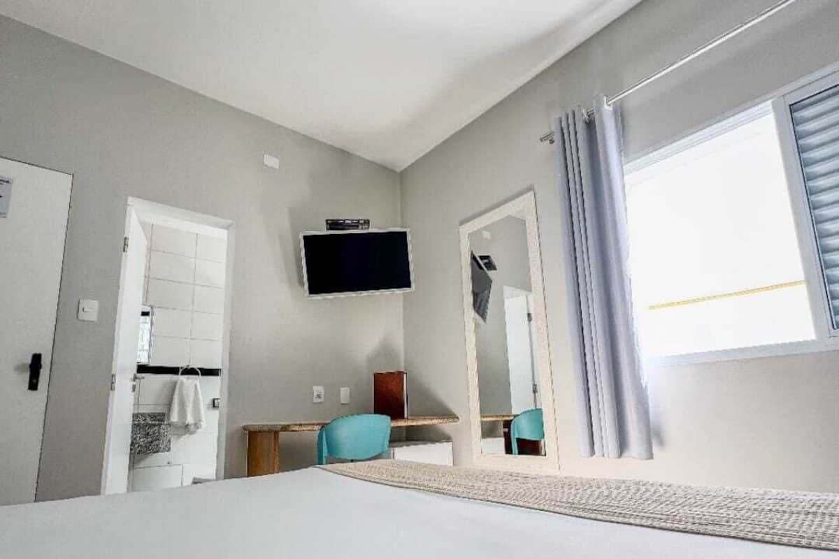 Habitación de hotel con una cama grande, un escritorio con silla, un televisor montado en la pared y una ventana con cortinas.