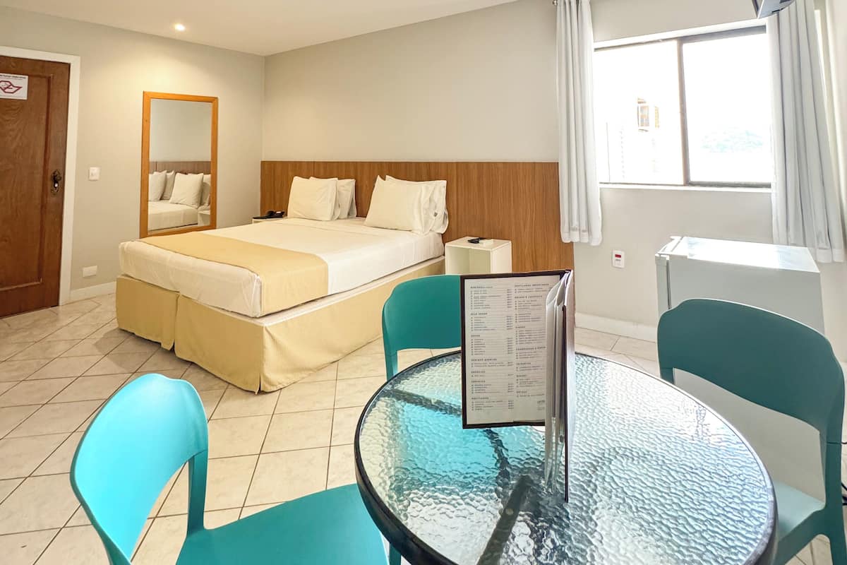 Una habitación de hotel con cama, una mesa con sillas, televisión y ventana con cortinas.