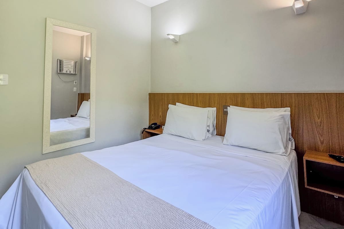 Una habitación de hotel con una cama grande, un cabecero de madera, una mesita de noche con teléfono y un espejo en la pared.