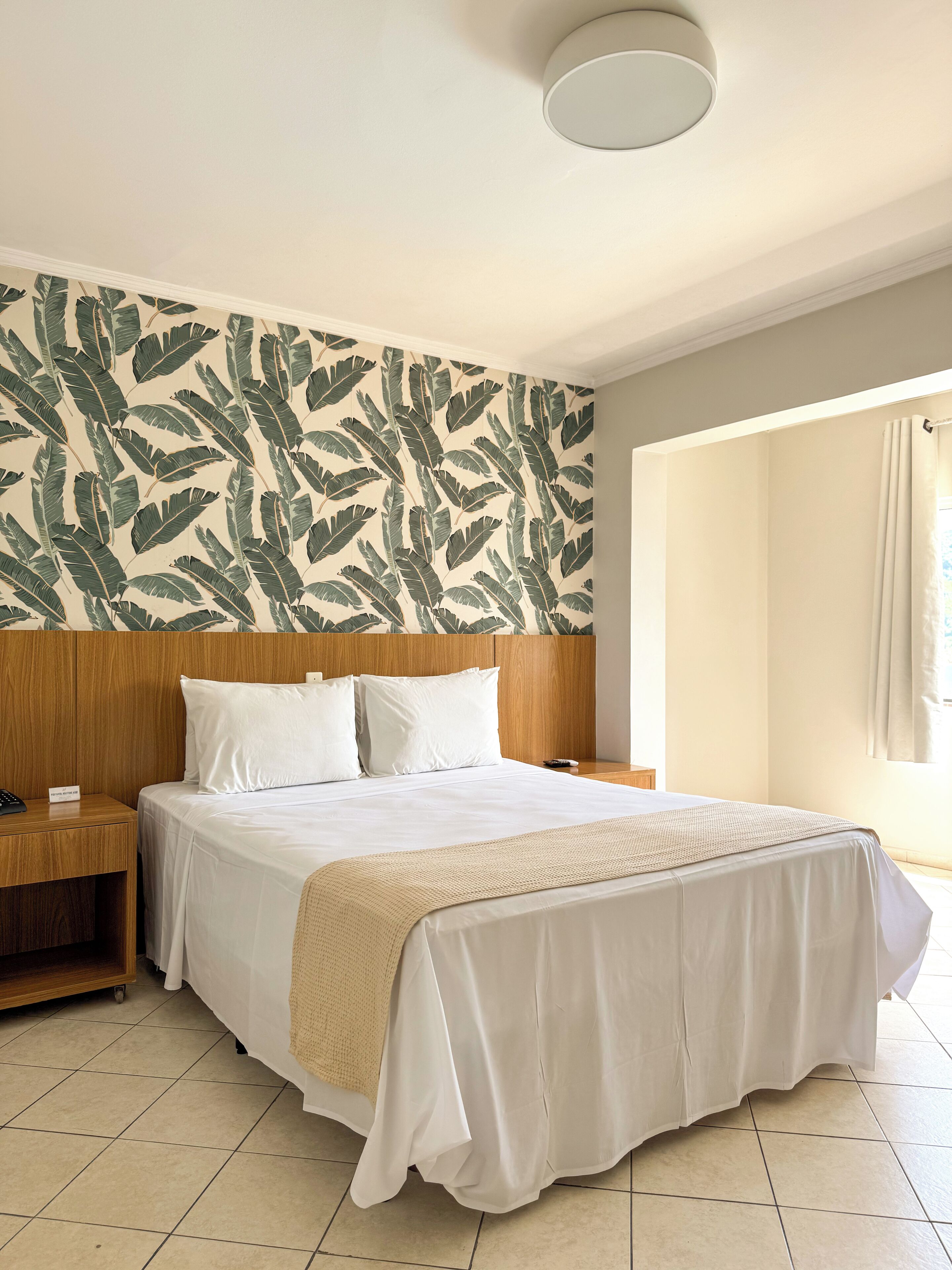 Una camera d'albergo con un letto grande, una testiera in legno, un comodino, un telefono e una parete con motivo a foglia.
