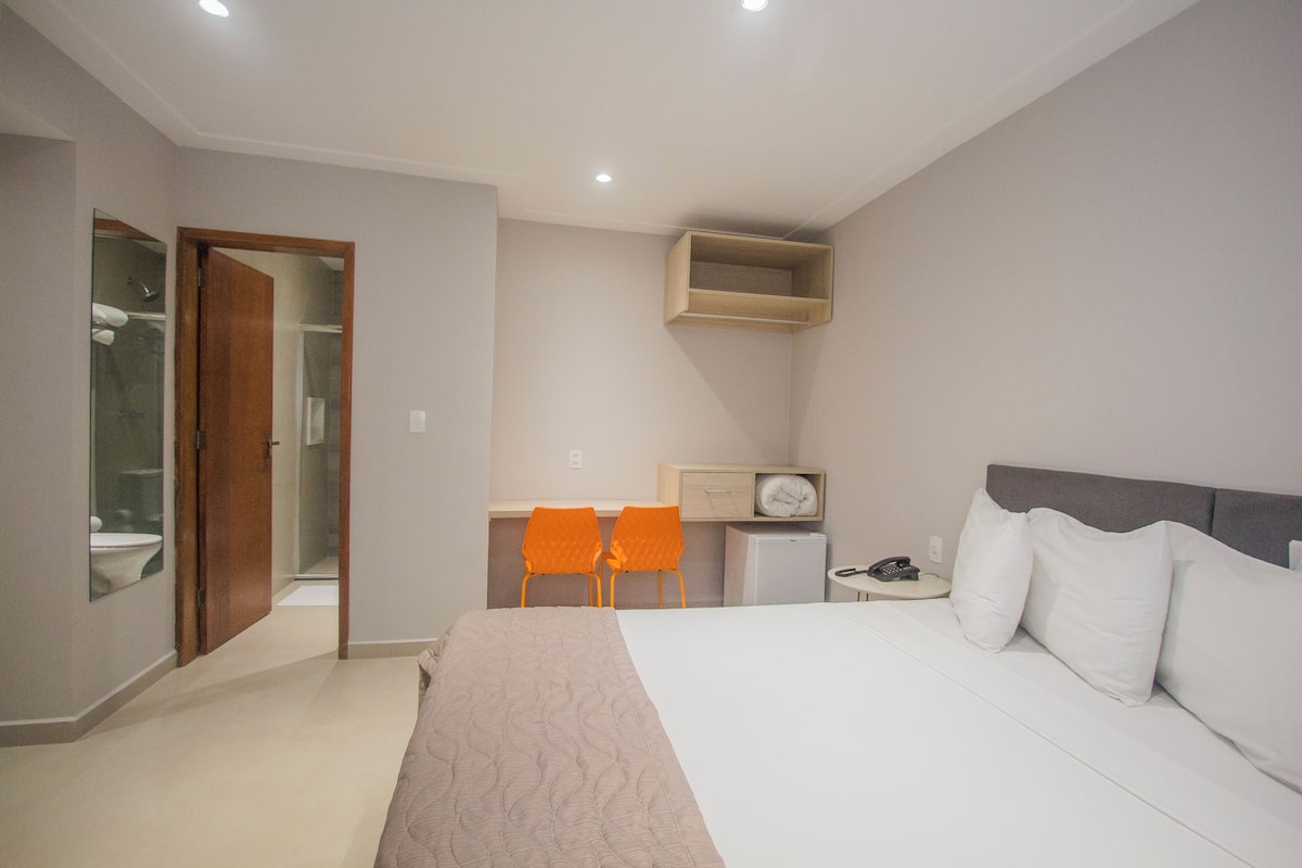 Un dormitorio con una cama grande, un escritorio con dos sillas, una mesita con un teléfono y un reloj en la pared.