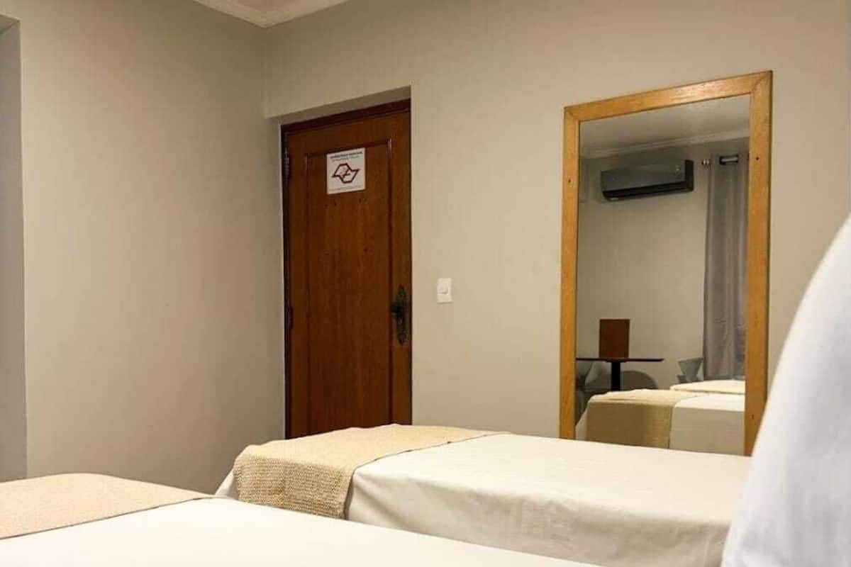 Habitación de hotel con dos camas individuales, una puerta de madera, un espejo y una mesita con lámpara.