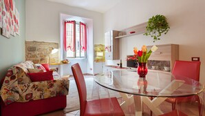 A modern living room with a glass dining table, red chairs, a sofa with patterned cushions, and a vase with flowers. - COZY CENTRAL APT CLOSE TO ST PETER BASILICA VATICAN MUSEUMS (Roma)