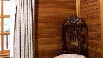 A corner room with wooden panel walls, a patterned curtain, and a wooden chair with a cushioned seat.