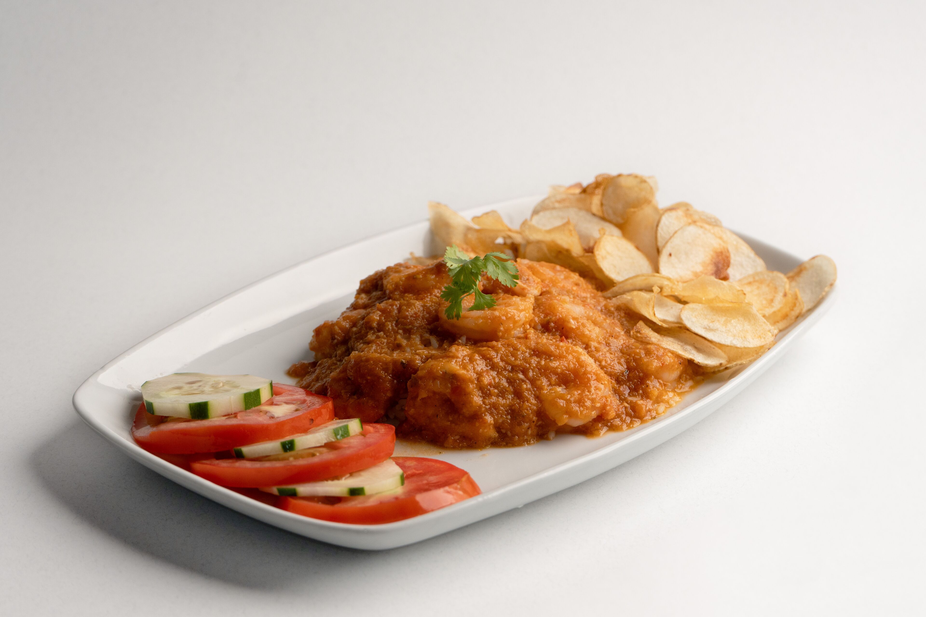 A white plate with a breaded chicken cutlet, sliced tomatoes, cucumbers, and chips.