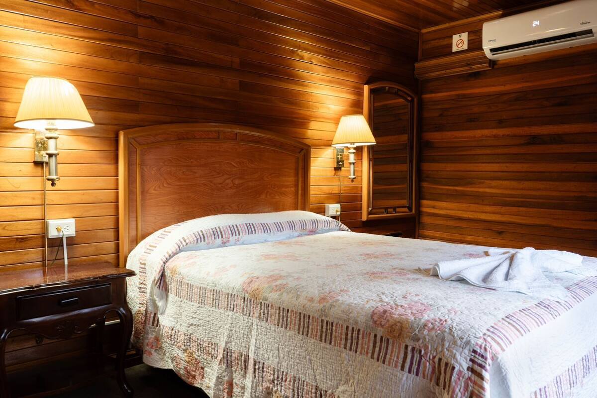 Een kamer met houten lambrisering, een bed, twee wandlampen en een airconditioning.