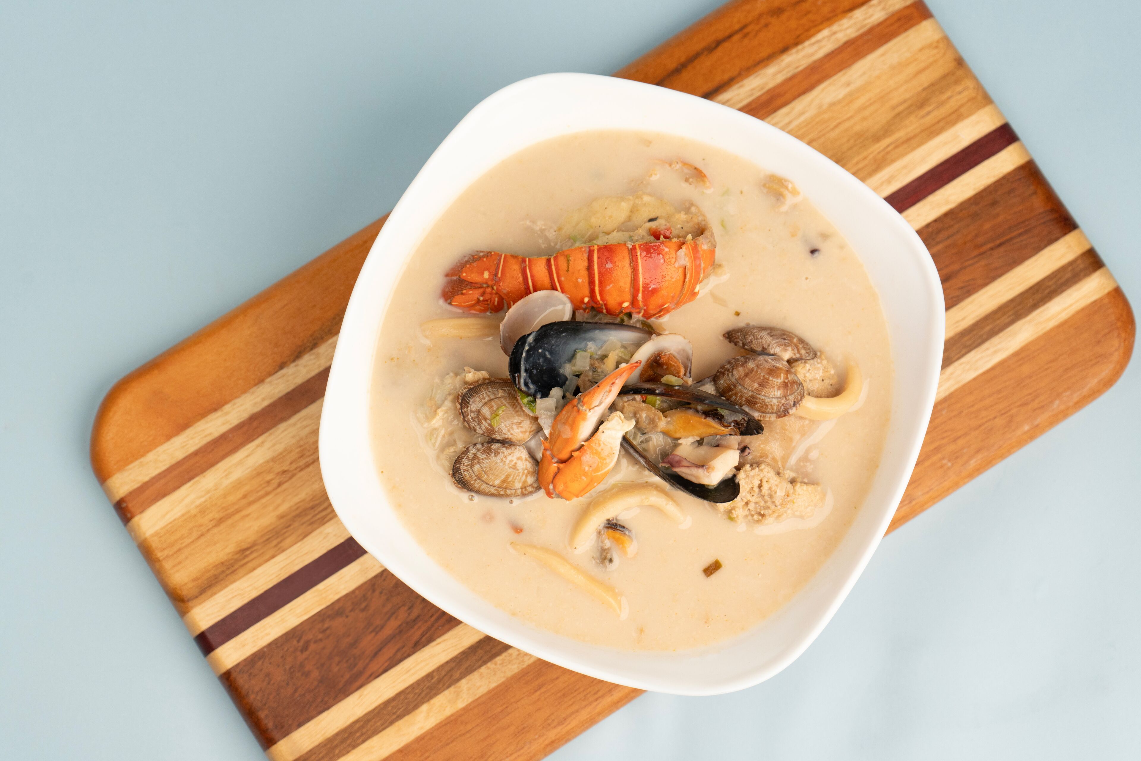 A bowl of seafood soup with various shellfish on a wooden board.