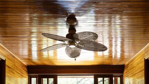 A room with a ceiling fan, two chairs, a bench, and large windows with a view of trees. - Santa Elena Lodge (Santa Elena)
