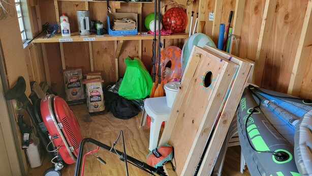 A small, wooden utility room with shelves containing various items like bags, containers, and tools.