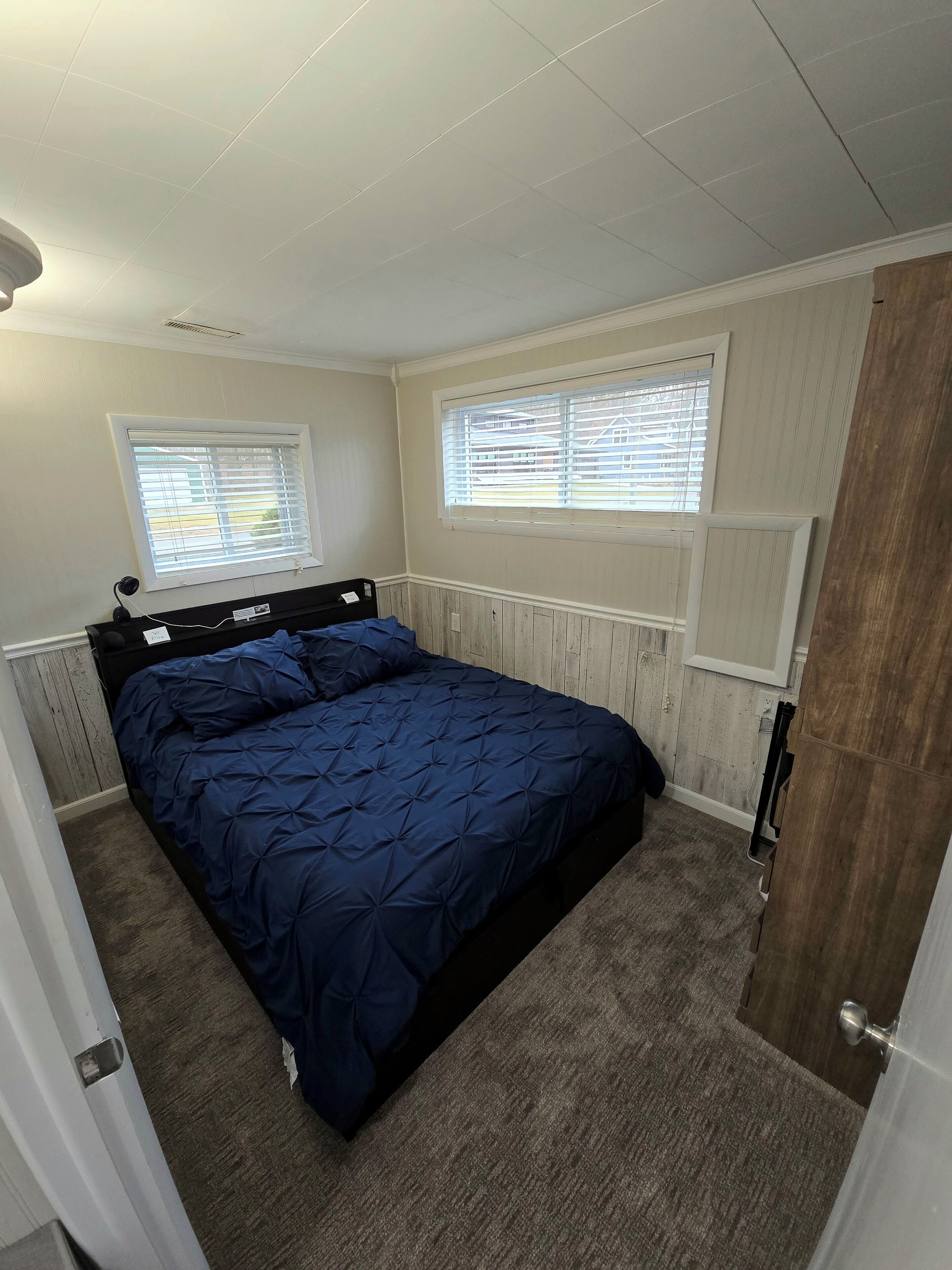 Un dormitorio con una cama, dos ventanas con persianas, un radiador y una puerta.