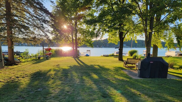 Zona verde con una parrilla, un banco y vista a un lago con barcos al fondo.
