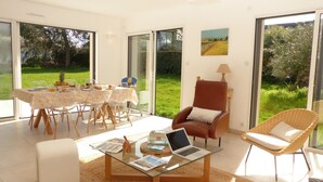 Un salon lumineux avec une table basse en verre, un ordinateur portable et un coin repas avec une table mise pour deux personnes.