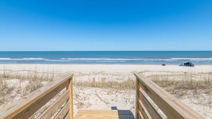 A wooden boardwalk leading to a beach with a clear view of the ocean.