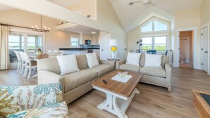A spacious living room with a high ceiling, a dining area, and a kitchen.