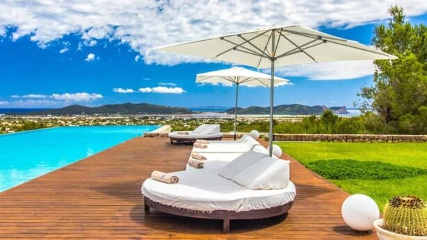Eine Holzterrasse mit Liegestühlen und Sonnenschirmen mit Blick auf einen Pool und eine malerische Landschaft.
