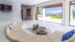 Ein modernes Wohnzimmer mit einer gebogenen Couch, einem flachbildfernseher an der Wand und einem großen Fenster mit Blick auf eine üppige Landschaft.