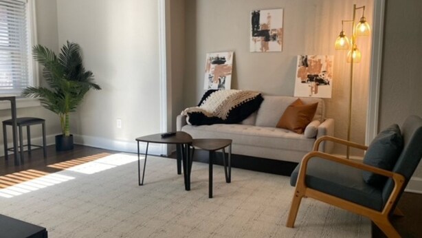 Una sala de estar con sofá, sillón, mesa de centro y planta en maceta.