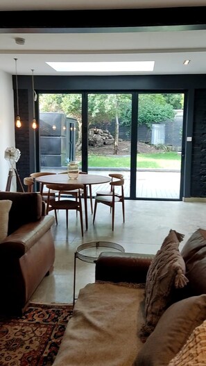 A modern living room with a sofa, a coffee table, and a dining table with chairs. There is a large window providing a view of the outdoors. - Remarkable 7-bed House in London (London)