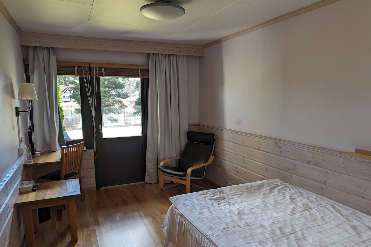 Une chambre d’hôtel comprenant un lit, un bureau avec une chaise, une fenêtre avec des rideaux et une vue sur l’extérieur.