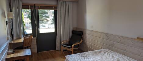 A hotel room with a bed, a desk with a chair, a window with curtains, and a view of the outside.