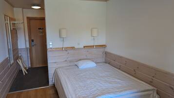 Une chambre d’hôtel avec une tête de lit en bois, un lit avec une literie blanche, deux lampes fixées au mur, une porte avec une pancarte et un plancher en bois.