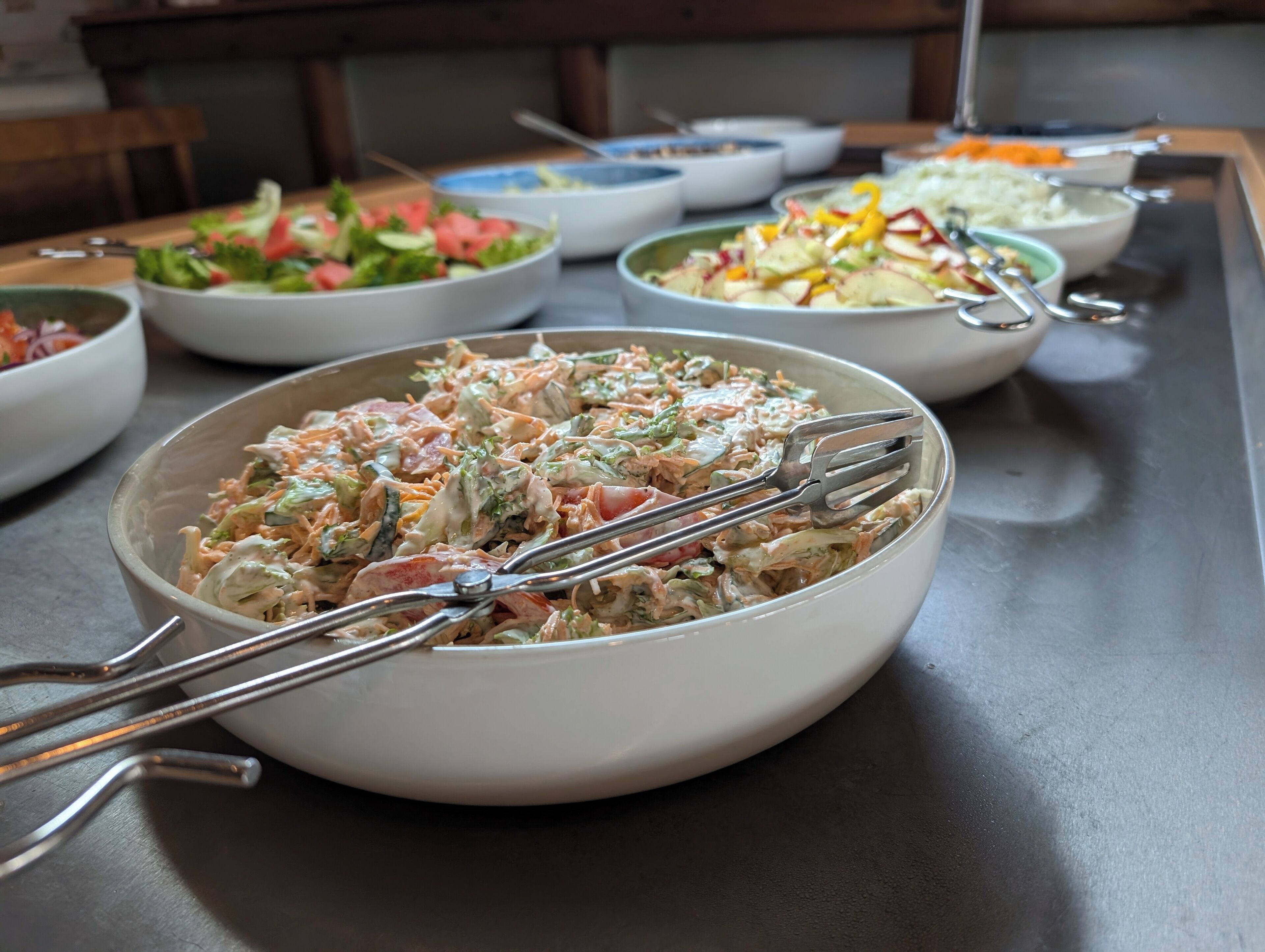 Een buffet met diverse gerechten, waaronder salades en een romige aardappelsalade.