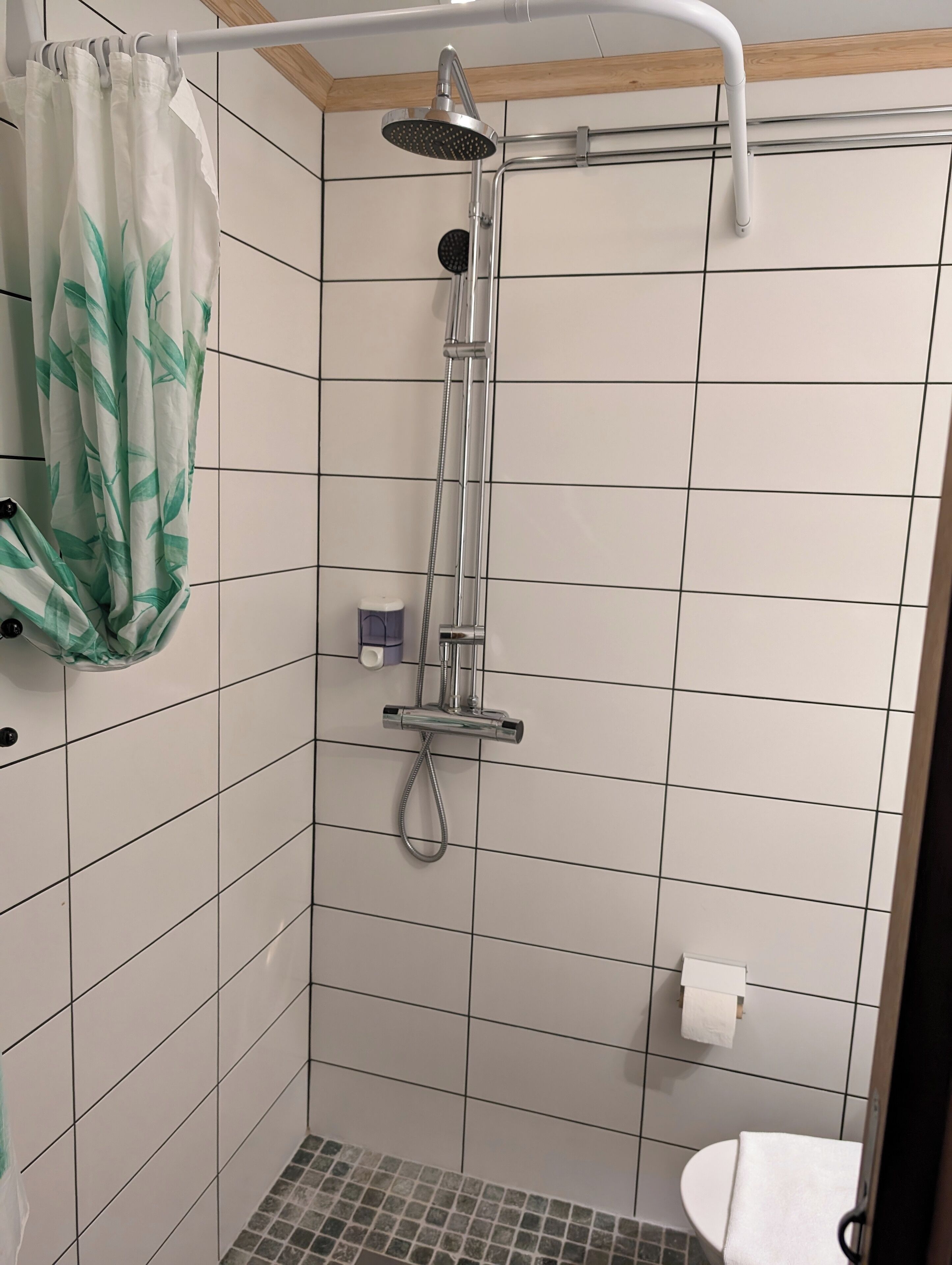 A small, tiled shower area with a handheld showerhead and a handheld shower attachment.