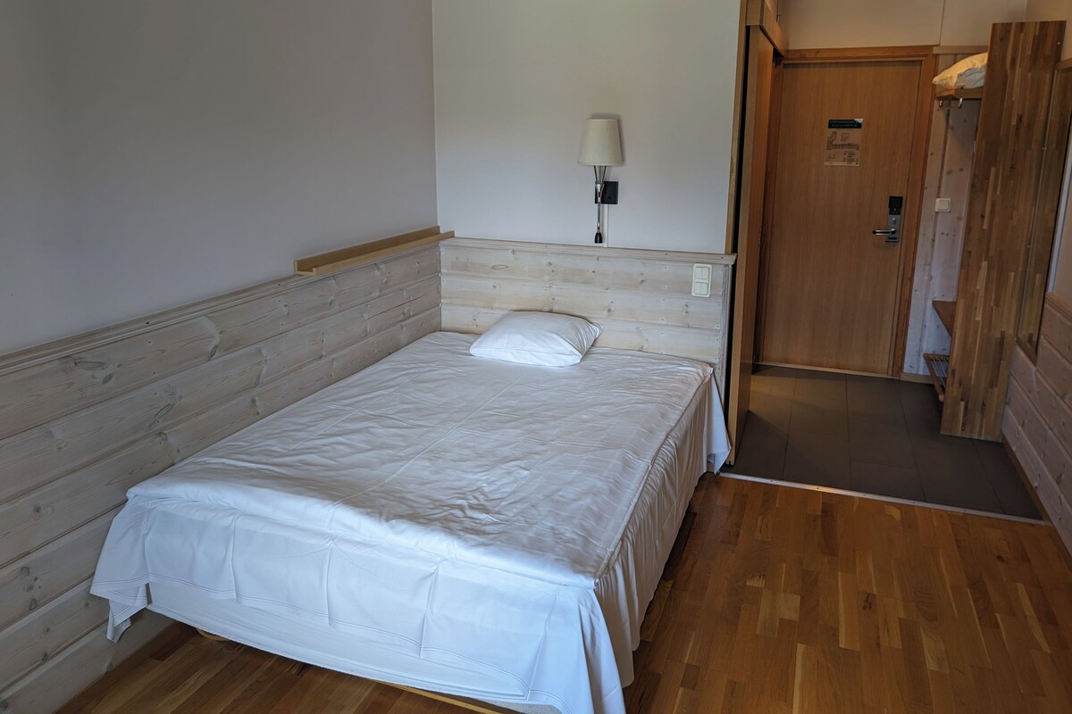 A single-bed room with a wooden headboard, a bedside lamp, and a door leading to a bathroom.