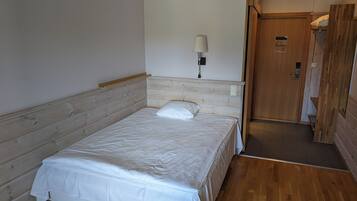 Une chambre avec un lit simple, une tête de lit en bois, une lampe de chevet et une porte donnant sur la salle de bain.