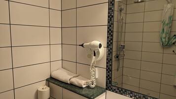 Ein Badezimmer mit Handtuchhalter, Handtrockner, Toilettenpapierhalter und einer Dusche mit gefliesten Wänden.