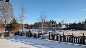 A snow-covered park with a wooden fence, trees, and a building in the background. - Värdshuset Flottaren (Vansbro)